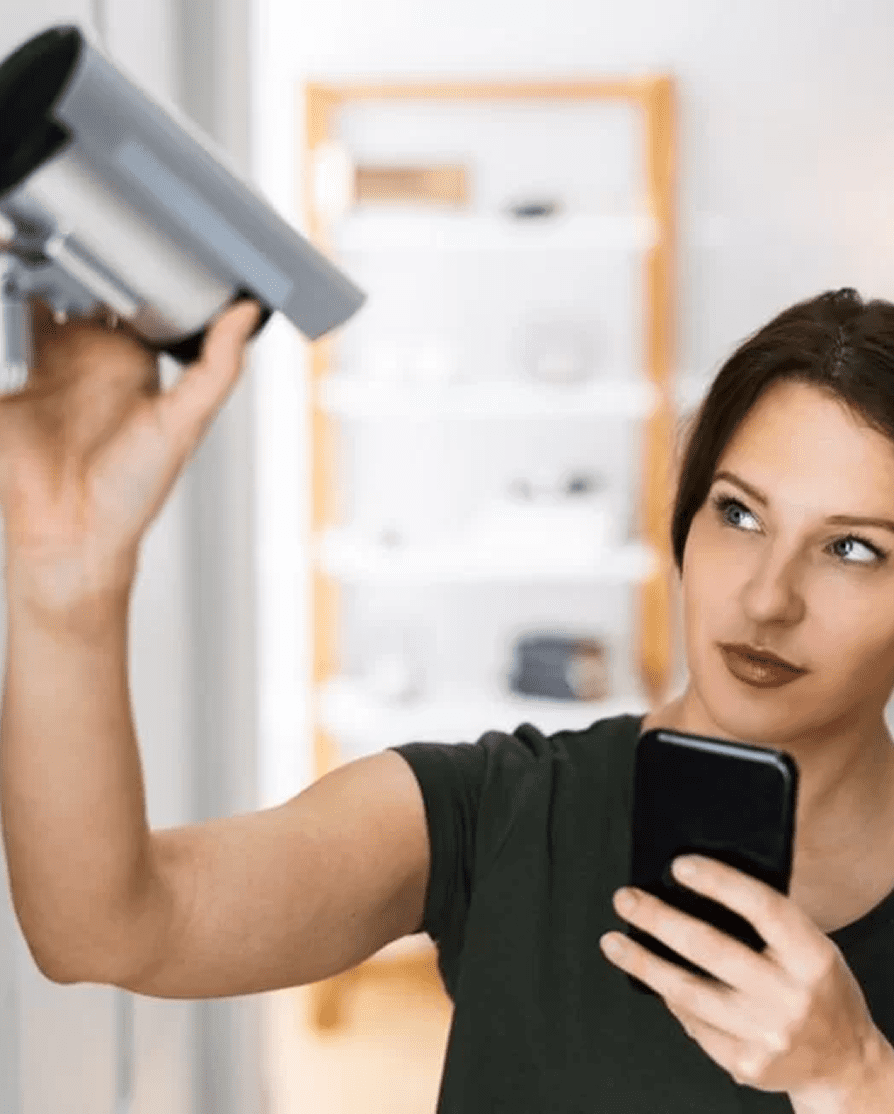 image (36) Woman configuring a CCTV camera while using a smartphone, showcasing home security setup for effective surveillance.